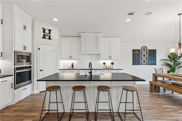 kitchen with a breakfast bar area, stainless steel appliances, a sink, visible vents, and dark countertops