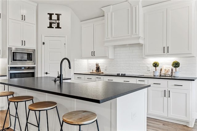 kitchen featuring tasteful backsplash, dark countertops, appliances with stainless steel finishes, light wood-style floors, and white cabinetry