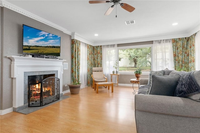 living room featuring visible vents, ornamental molding, wood finished floors, a lit fireplace, and baseboards