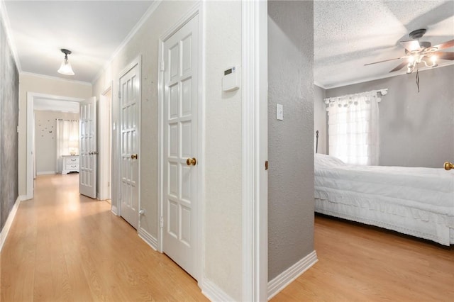 hallway featuring baseboards, a textured wall, light wood-style flooring, and crown molding