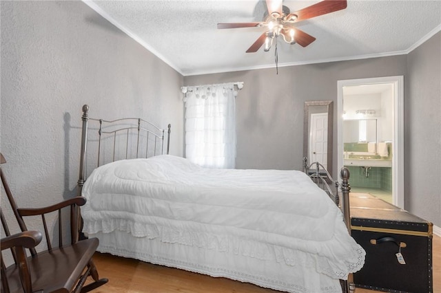 bedroom featuring a textured ceiling, a textured wall, ensuite bathroom, wood finished floors, and crown molding