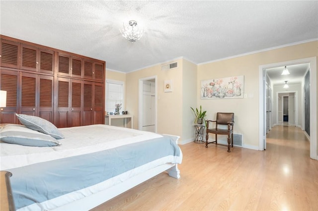 bedroom featuring a textured ceiling, ornamental molding, light wood-type flooring, and visible vents