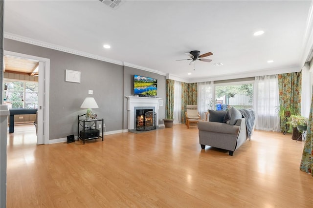 living area with a warm lit fireplace, light wood finished floors, visible vents, and crown molding