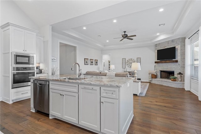 kitchen featuring a sink, a tray ceiling, open floor plan, appliances with stainless steel finishes, and white cabinets