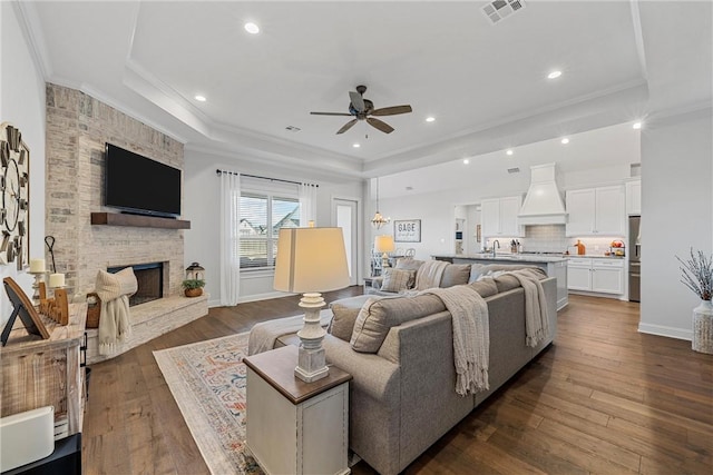 living room with visible vents, dark wood-type flooring, ornamental molding, a tray ceiling, and a fireplace