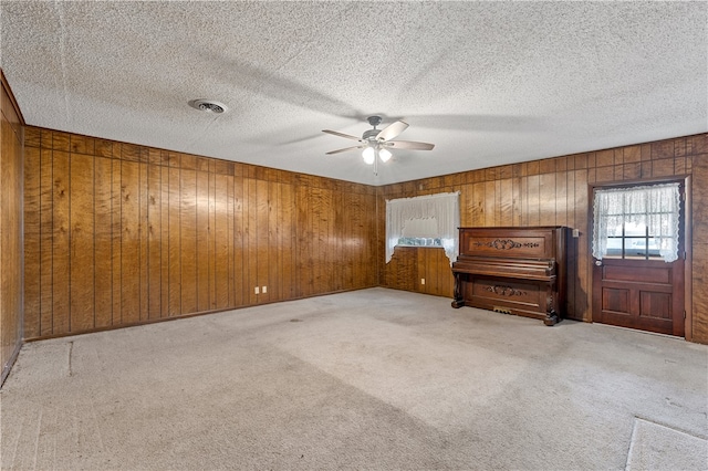 carpeted spare room with ceiling fan, wood walls, and a textured ceiling