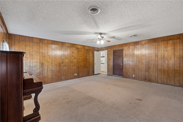 spare room with light carpet, a textured ceiling, ceiling fan, and wood walls