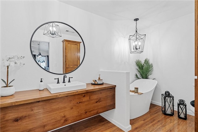 bathroom with a freestanding bath, an inviting chandelier, and wood finished floors