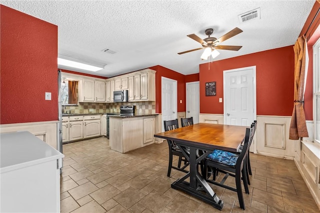 kitchen with a ceiling fan, a wainscoted wall, visible vents, appliances with stainless steel finishes, and a textured ceiling