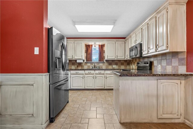 kitchen with a sink, stainless steel appliances, dark stone counters, a peninsula, and decorative backsplash