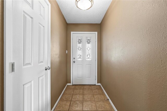 doorway with baseboards, a textured ceiling, light tile patterned flooring, and a textured wall