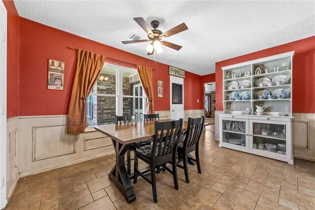 dining space featuring a wainscoted wall, a textured ceiling, visible vents, and a ceiling fan