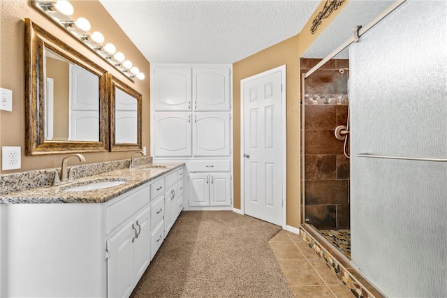 bathroom featuring a sink, a textured ceiling, double vanity, and a tile shower