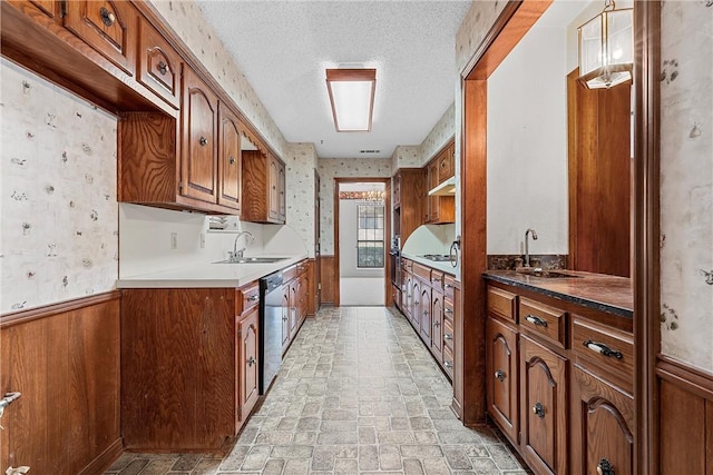 kitchen featuring dishwasher, sink, wood walls, and a textured ceiling