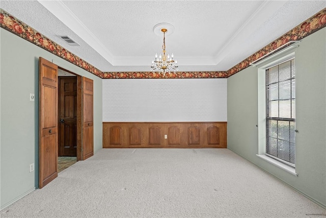 carpeted empty room with a textured ceiling, a tray ceiling, crown molding, and a notable chandelier