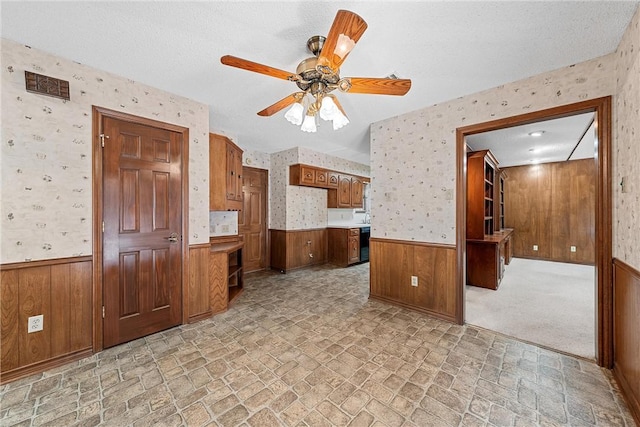 kitchen featuring light carpet, ceiling fan, a textured ceiling, and wooden walls