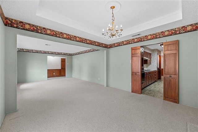 carpeted spare room with a textured ceiling, a raised ceiling, and a chandelier