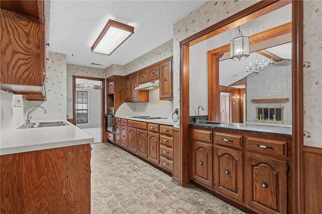 kitchen featuring decorative light fixtures, sink, black gas cooktop, stainless steel oven, and a brick fireplace