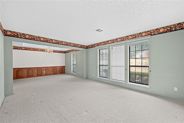 carpeted empty room featuring a chandelier and a textured ceiling