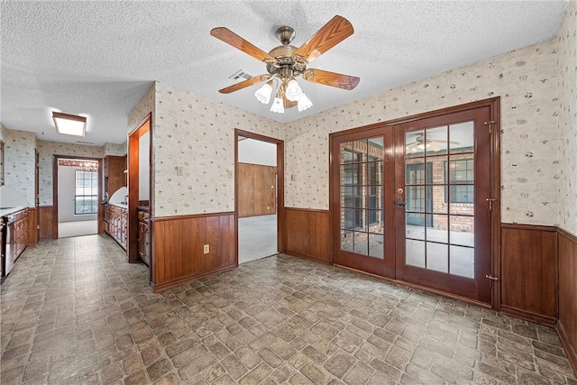 unfurnished room featuring a textured ceiling, ceiling fan, french doors, and wooden walls