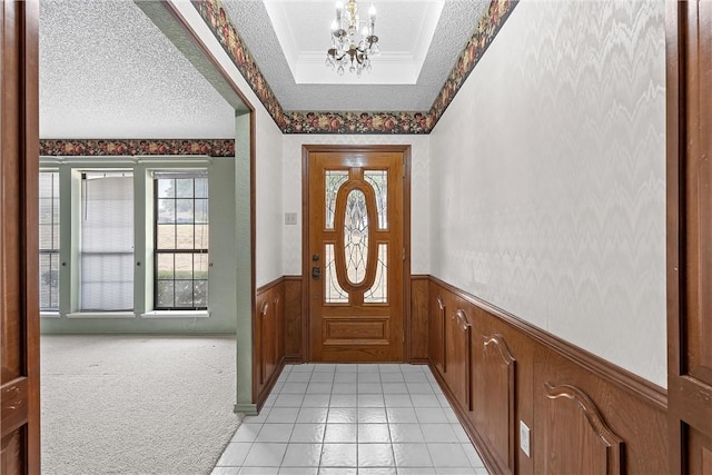 entryway with light carpet, a tray ceiling, a textured ceiling, a chandelier, and crown molding