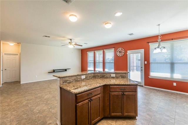 kitchen with pendant lighting, ceiling fan with notable chandelier, a kitchen island, and light stone counters