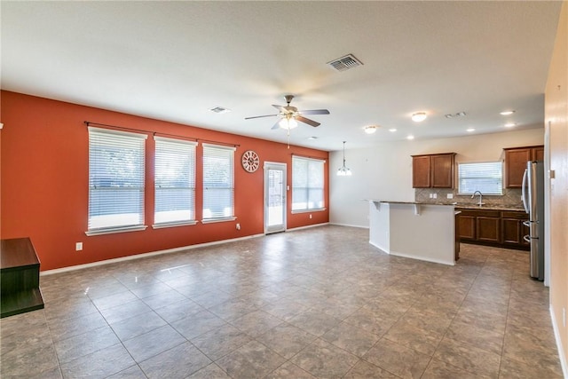 kitchen featuring tasteful backsplash, ceiling fan, a breakfast bar area, a kitchen island, and stainless steel refrigerator