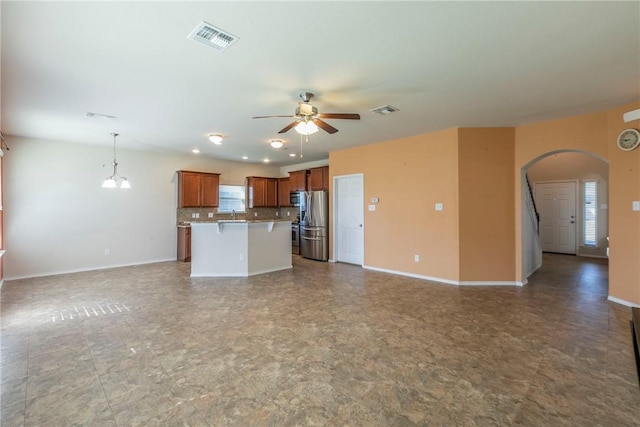 kitchen with a kitchen bar, appliances with stainless steel finishes, ceiling fan with notable chandelier, a kitchen island, and hanging light fixtures