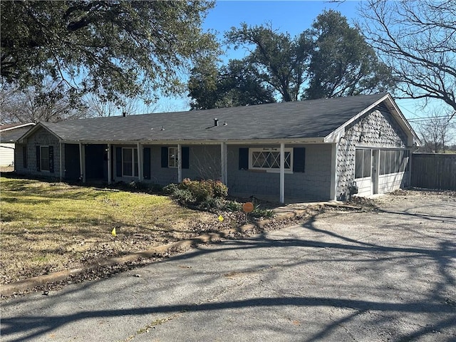 ranch-style home featuring gravel driveway, concrete block siding, and a front yard