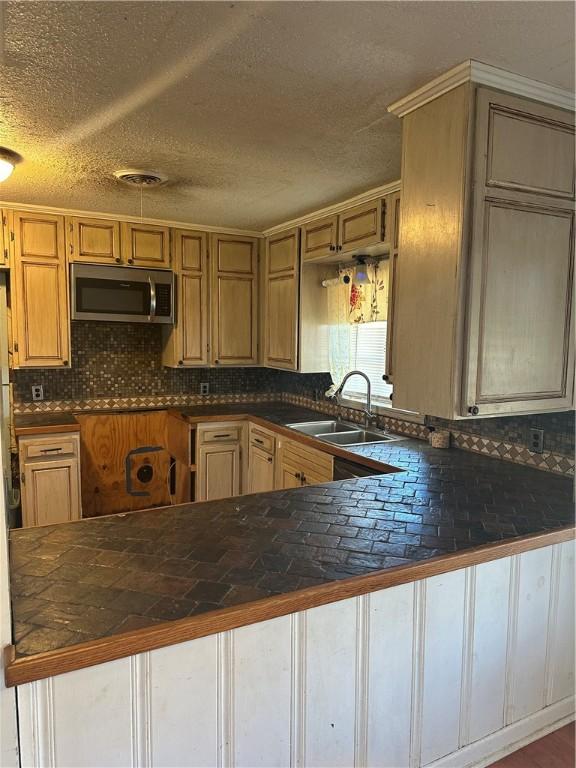 kitchen with tasteful backsplash, dark countertops, stainless steel microwave, a sink, and a peninsula