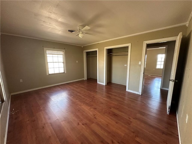 unfurnished bedroom with baseboards, ornamental molding, dark wood finished floors, and two closets