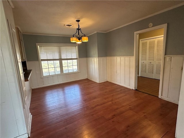 unfurnished dining area with crown molding, a chandelier, wainscoting, and dark wood finished floors