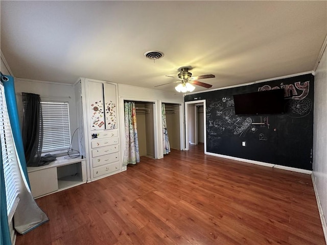 unfurnished bedroom featuring wood finished floors, a ceiling fan, visible vents, two closets, and crown molding