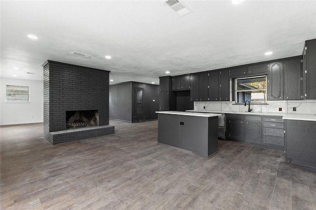 kitchen with decorative backsplash, a brick fireplace, dark wood-type flooring, sink, and a kitchen island