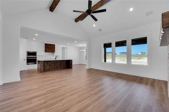 unfurnished living room featuring beamed ceiling, light wood-type flooring, high vaulted ceiling, and ceiling fan with notable chandelier