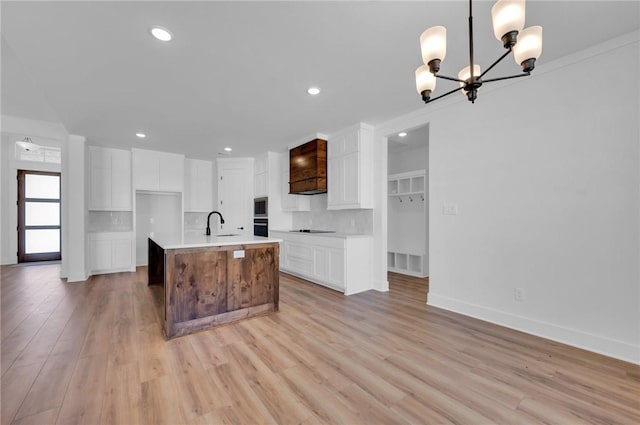 kitchen with white cabinetry, a center island with sink, hanging light fixtures, and light hardwood / wood-style floors