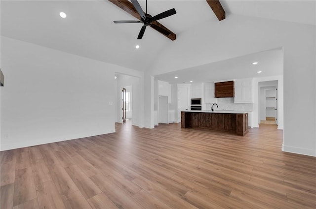 unfurnished living room featuring ceiling fan, sink, high vaulted ceiling, light hardwood / wood-style flooring, and beamed ceiling