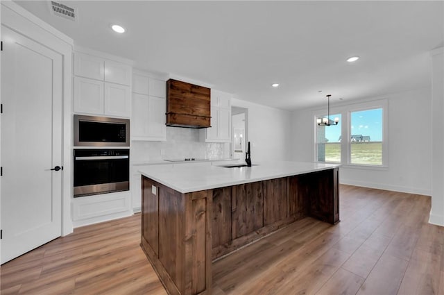 kitchen featuring a notable chandelier, light hardwood / wood-style floors, an island with sink, and appliances with stainless steel finishes