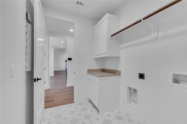 washroom featuring hookup for an electric dryer, washer hookup, light hardwood / wood-style flooring, and cabinets