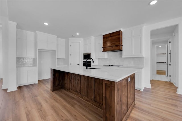 kitchen featuring white cabinetry, stainless steel microwave, an island with sink, and light wood-type flooring