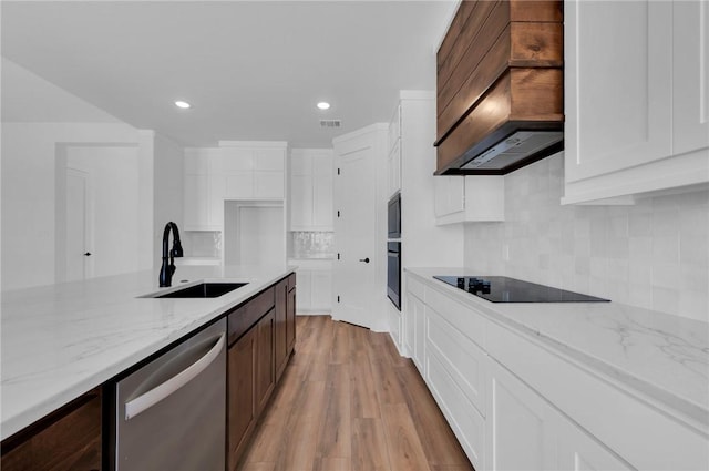 kitchen featuring light stone countertops, sink, premium range hood, light hardwood / wood-style floors, and appliances with stainless steel finishes