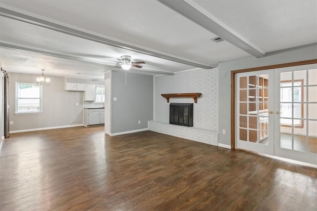 unfurnished living room with french doors, ceiling fan with notable chandelier, dark wood-type flooring, beam ceiling, and a fireplace