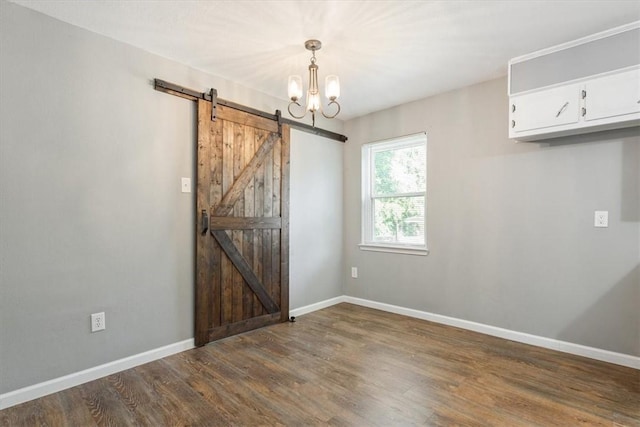 empty room with a notable chandelier, dark hardwood / wood-style floors, and a barn door