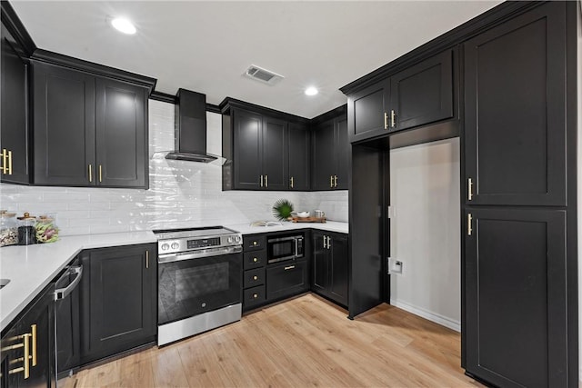 kitchen featuring tasteful backsplash, wall chimney exhaust hood, light wood-type flooring, and appliances with stainless steel finishes