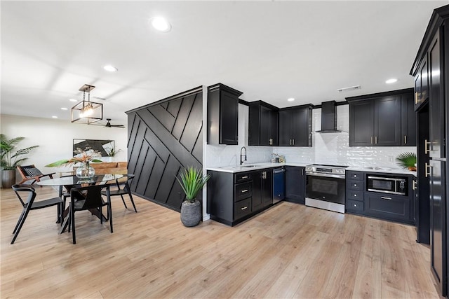 kitchen with appliances with stainless steel finishes, light hardwood / wood-style floors, pendant lighting, and wall chimney range hood