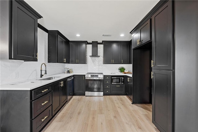 kitchen featuring wall chimney range hood, sink, decorative backsplash, light wood-type flooring, and appliances with stainless steel finishes