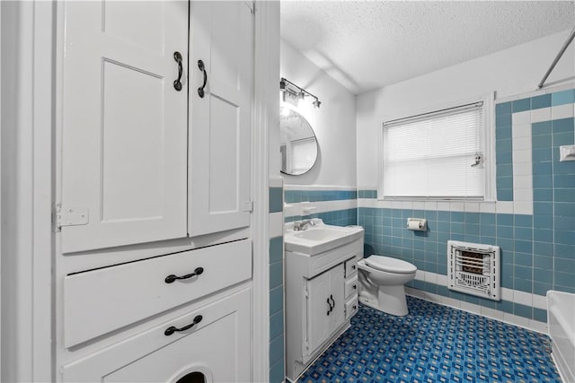 bathroom with vanity, toilet, a textured ceiling, tile walls, and heating unit