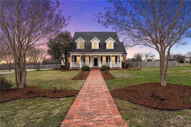 cape cod home with covered porch, a lawn, and fence