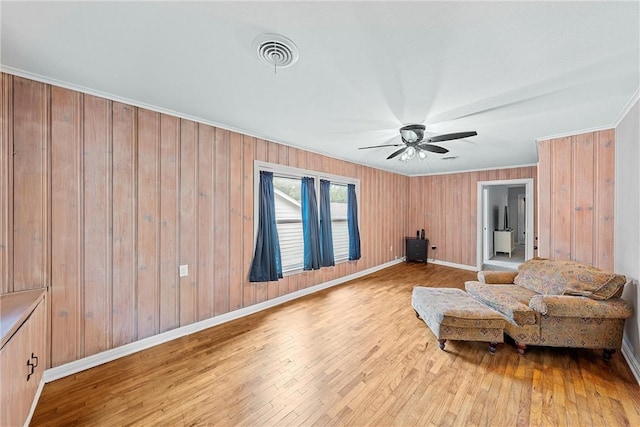 living area with light wood-type flooring, wooden walls, ceiling fan, and ornamental molding