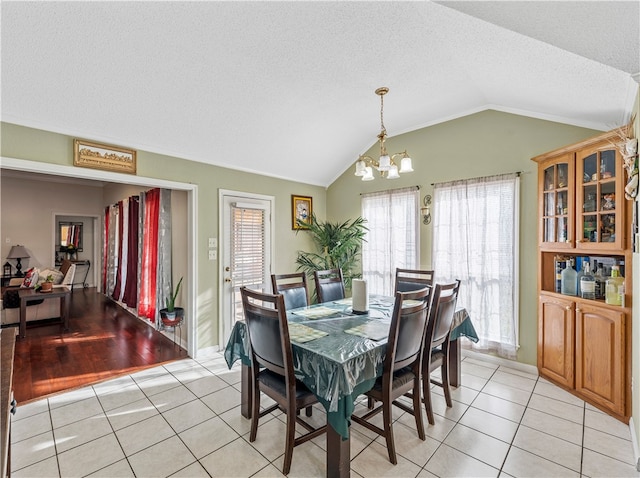 dining room featuring an inviting chandelier, vaulted ceiling, light tile patterned floors, and a textured ceiling